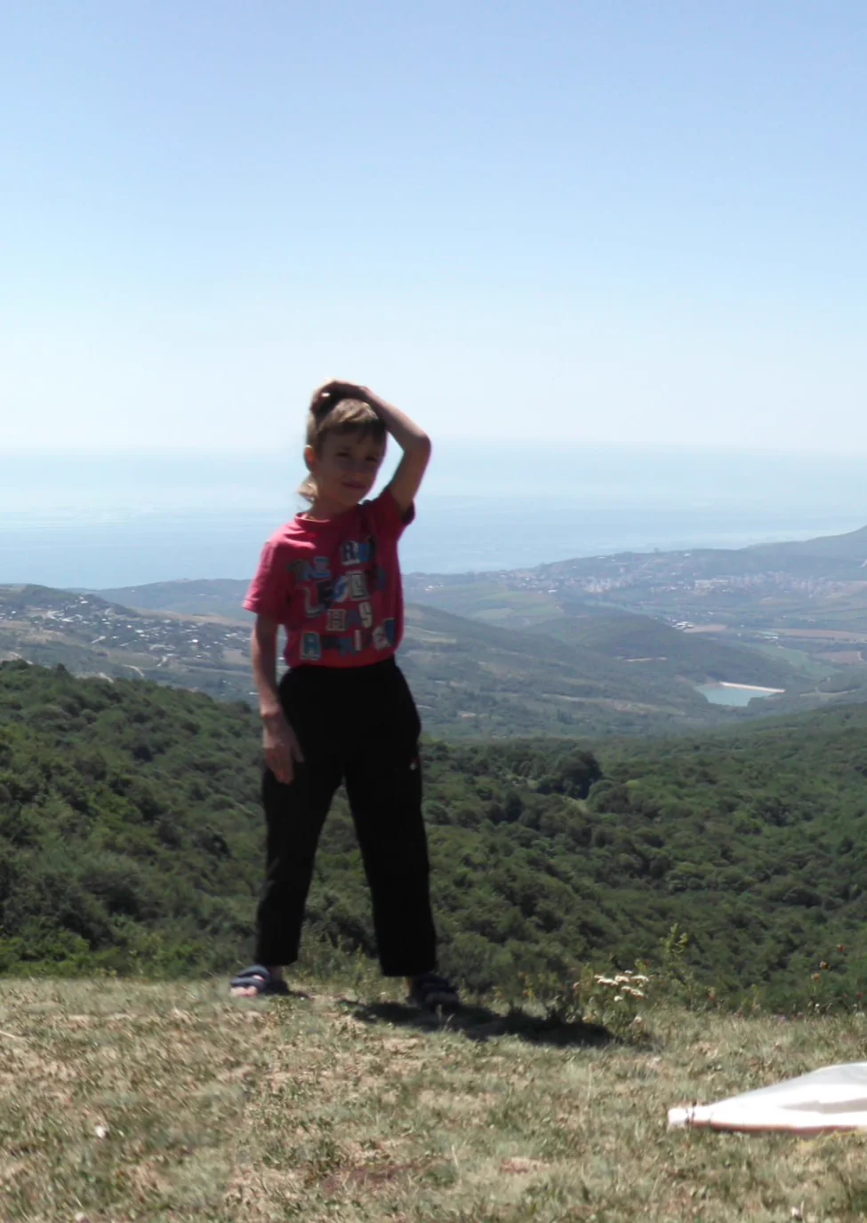 Me as a small boy on a hilltop, one hand on my head, with green hills and a hazy sea behind.