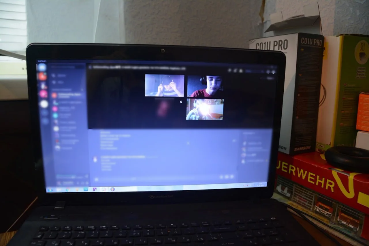 A laptop on a desk, its screen once a video call with friends, now worn away to dark with a few faint squares left.