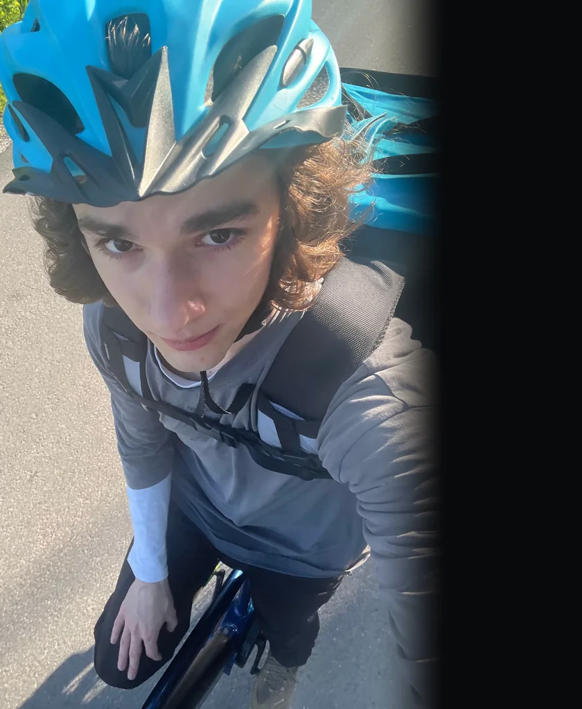 A selfie of me riding a bicycle in a blue helmet, with a blue delivery bag on my back.